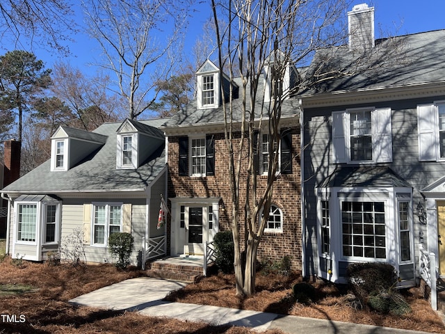 cape cod-style house featuring brick siding and a chimney