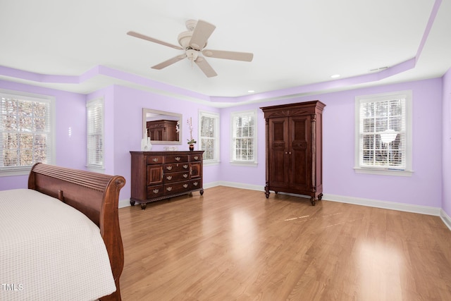 bedroom featuring light wood-style floors, a tray ceiling, multiple windows, and baseboards