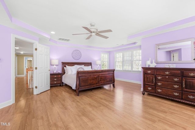 bedroom featuring light wood finished floors, baseboards, visible vents, ceiling fan, and a tray ceiling