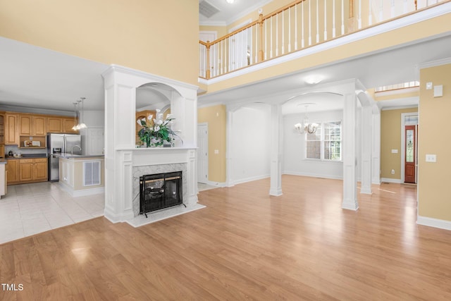 unfurnished living room featuring light wood-style flooring, a high ceiling, a fireplace, ornamental molding, and decorative columns