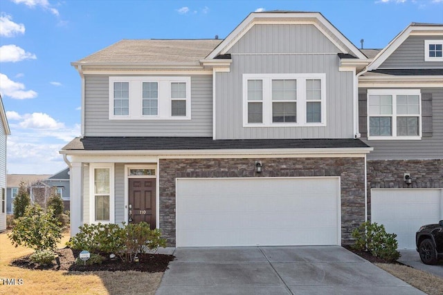 view of front facade featuring driveway, a garage, a shingled roof, stone siding, and board and batten siding