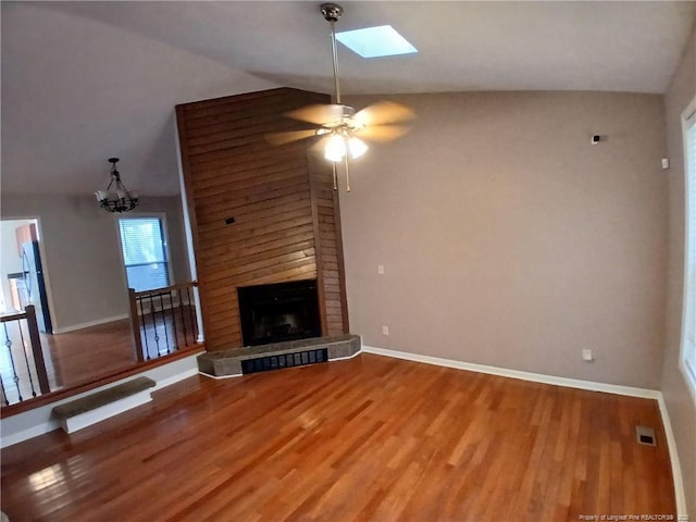 unfurnished living room with visible vents, a large fireplace, wood finished floors, vaulted ceiling with skylight, and baseboards