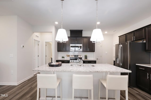 kitchen featuring light stone counters, pendant lighting, stainless steel appliances, an island with sink, and a kitchen breakfast bar