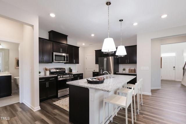 kitchen with a breakfast bar, decorative light fixtures, appliances with stainless steel finishes, an island with sink, and light stone countertops