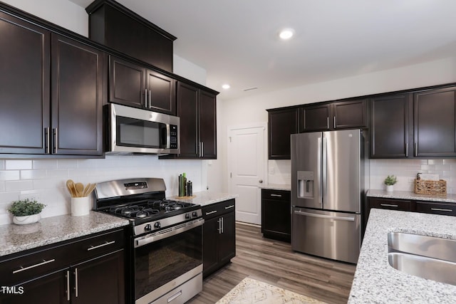 kitchen featuring light stone counters, stainless steel appliances, dark brown cabinets, light wood-style floors, and backsplash