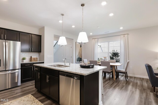 kitchen featuring pendant lighting, a center island with sink, stainless steel appliances, tasteful backsplash, and a sink