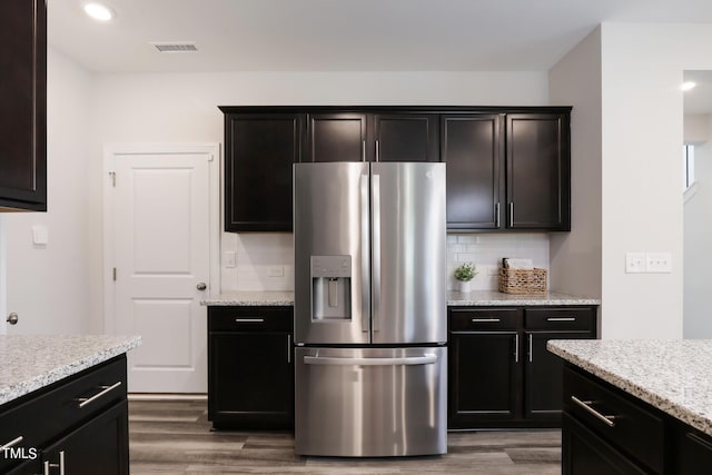 kitchen with dark wood-style flooring, stainless steel refrigerator with ice dispenser, visible vents, and decorative backsplash