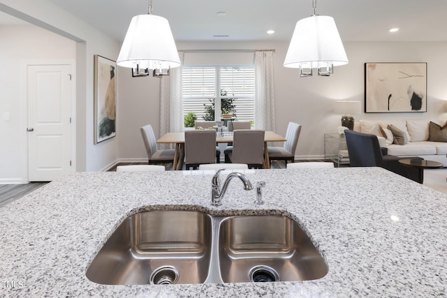 kitchen with recessed lighting, hanging light fixtures, a sink, light stone countertops, and baseboards