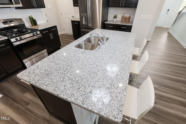 kitchen featuring a center island with sink, light stone counters, a breakfast bar, stainless steel appliances, and a sink