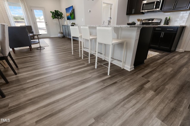 kitchen featuring a breakfast bar, dark wood-style flooring, a center island with sink, appliances with stainless steel finishes, and light stone countertops