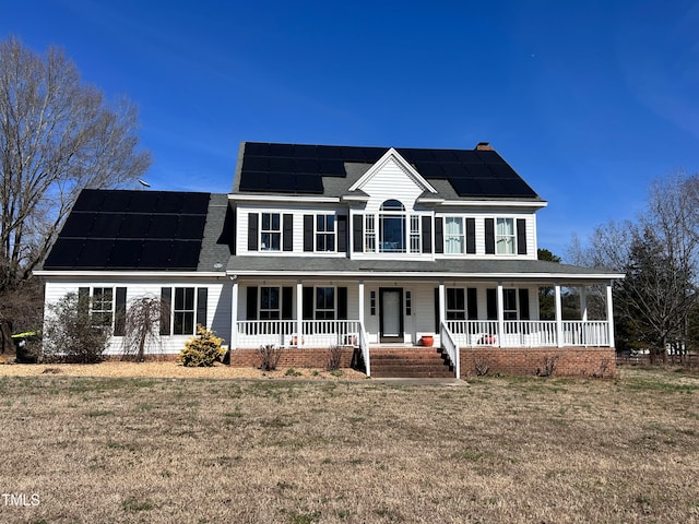 colonial home with a shingled roof, a front yard, covered porch, and solar panels