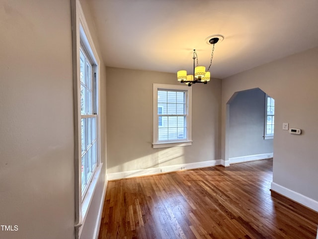 unfurnished dining area with an inviting chandelier, wood finished floors, and a healthy amount of sunlight