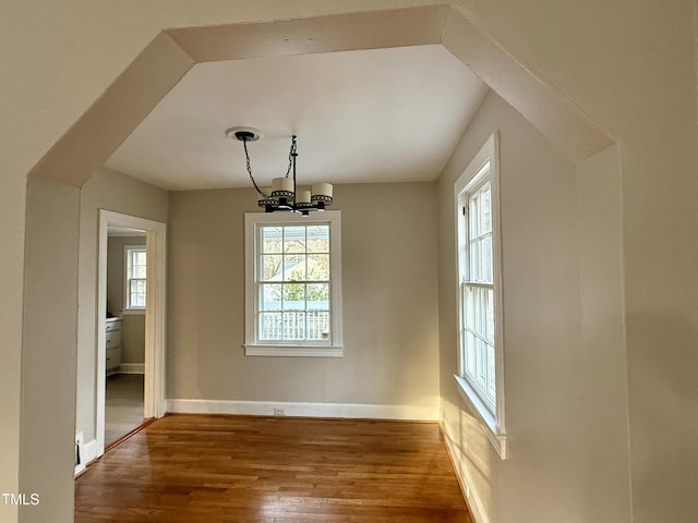 unfurnished dining area featuring a notable chandelier, plenty of natural light, baseboards, and wood finished floors