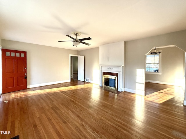 unfurnished living room with ceiling fan with notable chandelier, a fireplace, baseboards, and wood finished floors