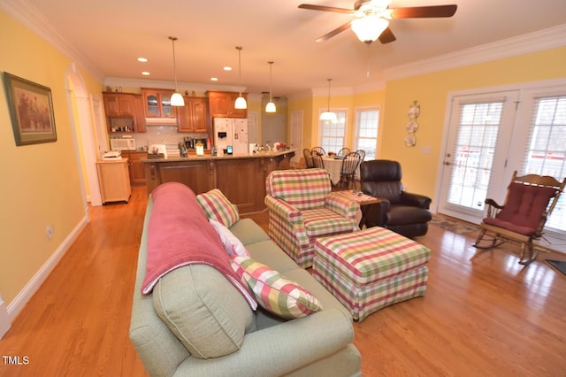 living room with ornamental molding, light wood finished floors, a ceiling fan, and baseboards