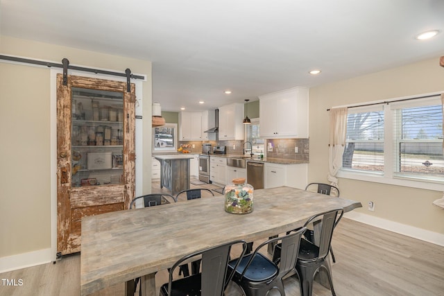 dining space with light wood-type flooring, a barn door, baseboards, and recessed lighting