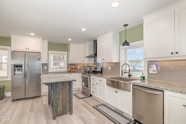 kitchen with light wood finished floors, white cabinets, wall chimney exhaust hood, appliances with stainless steel finishes, and a sink