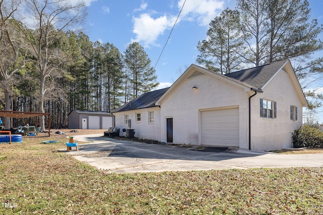 view of side of home with an attached garage, cooling unit, brick siding, an outdoor structure, and concrete driveway