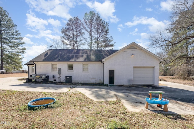 view of side of home with aphalt driveway, brick siding, roof with shingles, central AC, and a garage