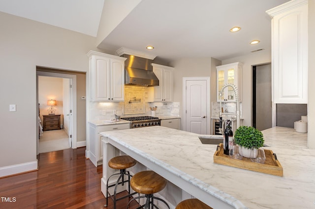 kitchen with a peninsula, white cabinets, a kitchen breakfast bar, backsplash, and wall chimney exhaust hood