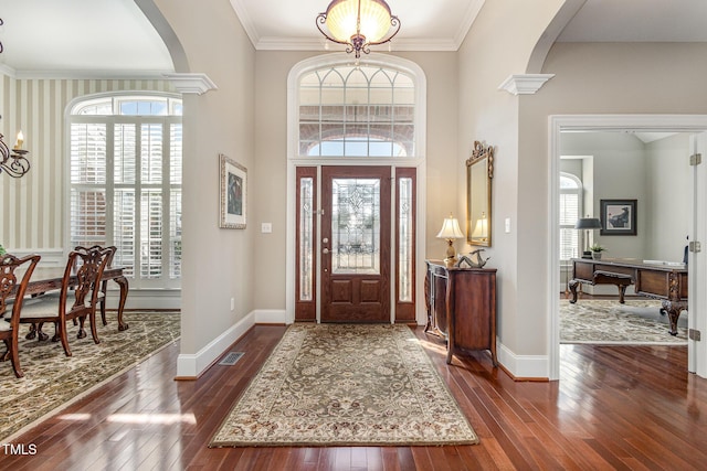 foyer entrance featuring arched walkways, visible vents, baseboards, and hardwood / wood-style flooring