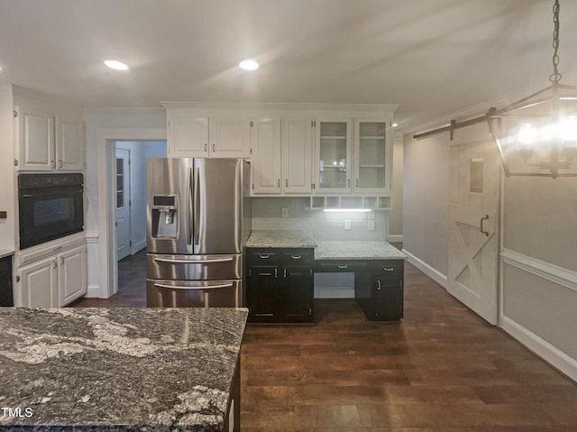 kitchen with black oven, a barn door, stainless steel fridge, and white cabinets