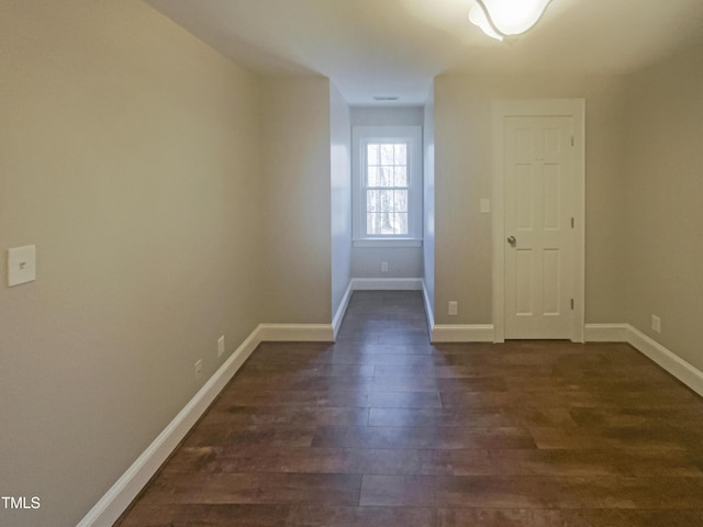 spare room with baseboards and dark wood-type flooring