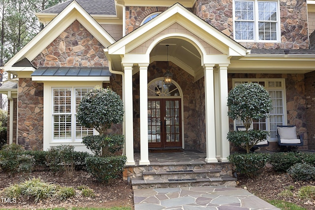 property entrance with french doors, stone siding, and roof with shingles