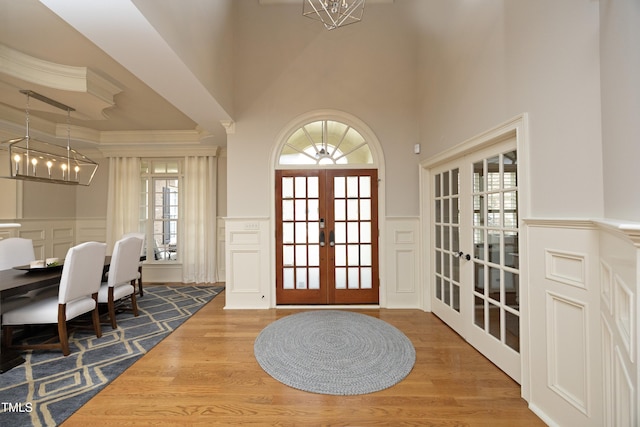 foyer with a chandelier, ornamental molding, french doors, wood finished floors, and a decorative wall