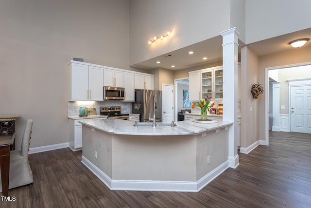 kitchen featuring white cabinets, a towering ceiling, a spacious island, dark wood-style floors, and stainless steel appliances