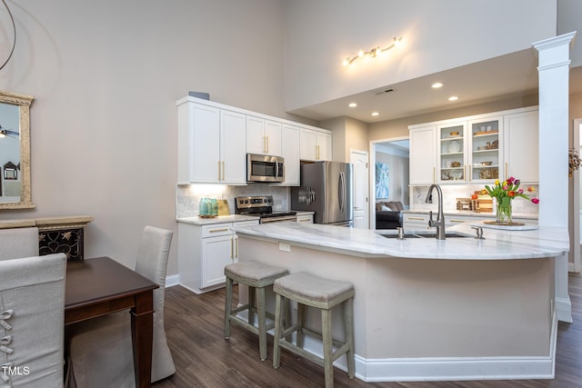 kitchen with light stone counters, appliances with stainless steel finishes, white cabinetry, a sink, and a kitchen bar