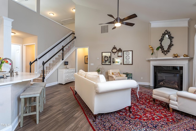 living room with dark wood-style floors, visible vents, stairway, a ceiling fan, and a glass covered fireplace