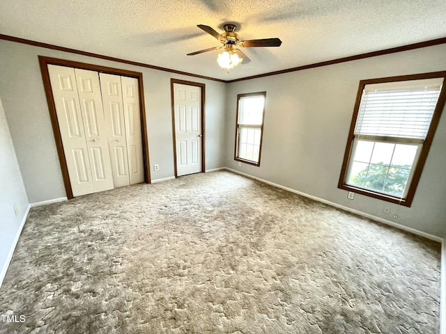 unfurnished bedroom with baseboards, crown molding, a textured ceiling, carpet floors, and multiple closets