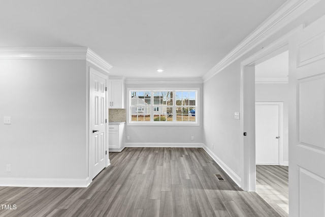 empty room featuring visible vents, crown molding, baseboards, and wood finished floors