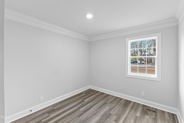 spare room with dark wood-style floors, visible vents, baseboards, and ornamental molding