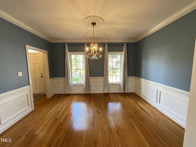 unfurnished dining area featuring a notable chandelier, wainscoting, crown molding, and wood finished floors