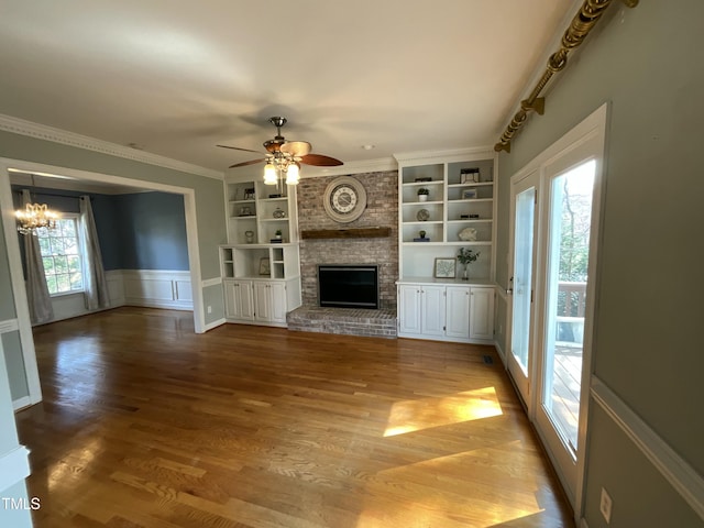 unfurnished living room with built in shelves, light wood-style floors, a fireplace, and ceiling fan with notable chandelier