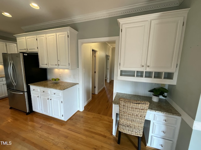 kitchen with light wood-type flooring, white cabinets, crown molding, and freestanding refrigerator