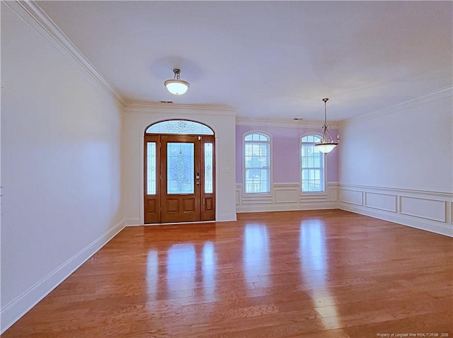 foyer featuring crown molding, a decorative wall, a wainscoted wall, and light wood-style floors