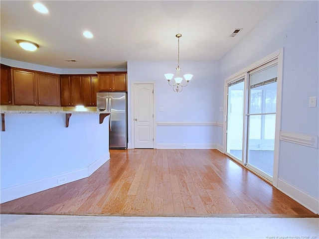 kitchen featuring hanging light fixtures, a breakfast bar, light wood-style floors, and stainless steel fridge with ice dispenser