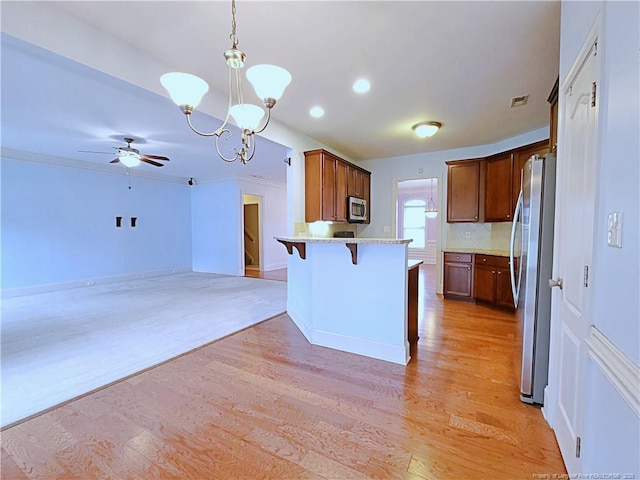 kitchen with a breakfast bar area, stainless steel appliances, open floor plan, hanging light fixtures, and brown cabinets