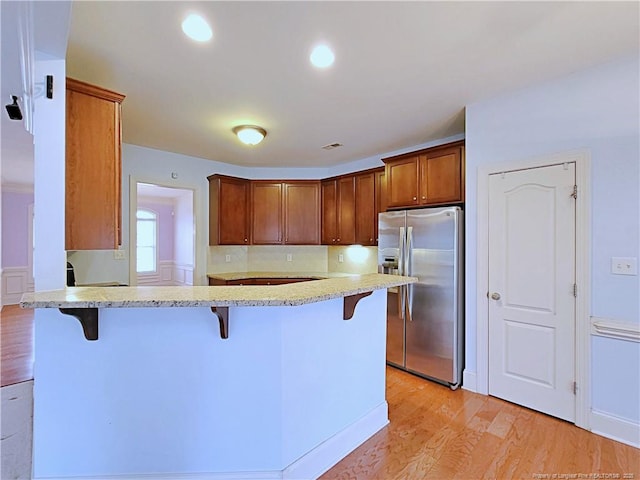 kitchen featuring a breakfast bar, brown cabinetry, light wood-style floors, a peninsula, and stainless steel fridge with ice dispenser