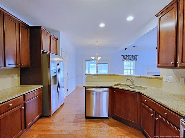 kitchen featuring light stone counters, stainless steel appliances, a peninsula, a sink, and decorative light fixtures