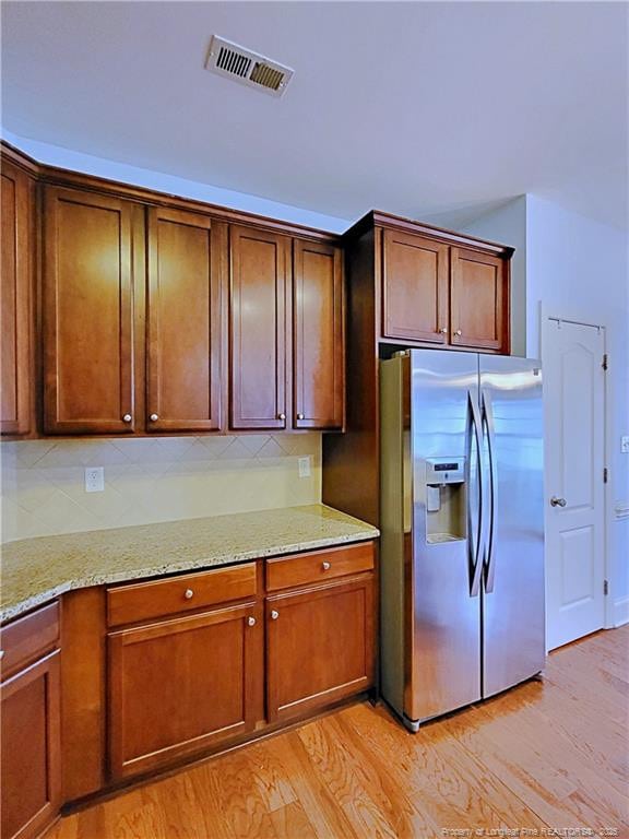 kitchen with light stone counters, stainless steel fridge, visible vents, and light wood-style floors