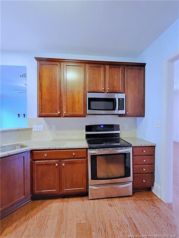 kitchen featuring a sink, appliances with stainless steel finishes, light stone countertops, light wood finished floors, and brown cabinetry