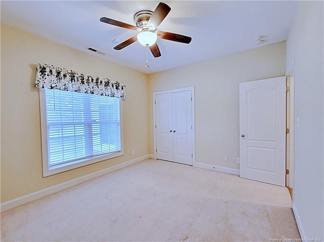 unfurnished bedroom featuring ceiling fan, light colored carpet, visible vents, baseboards, and a closet