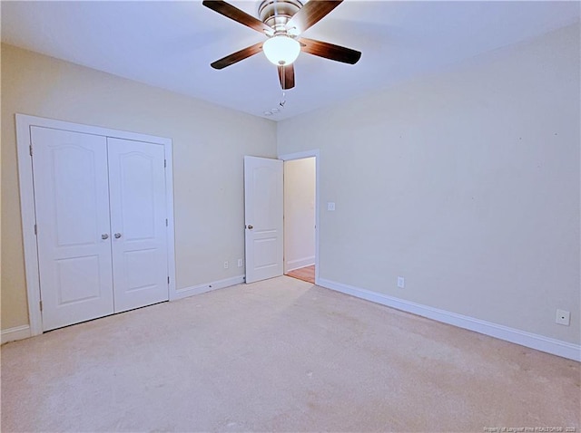 unfurnished bedroom with a closet, light colored carpet, ceiling fan, and baseboards