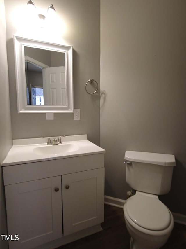 half bath with baseboards, toilet, wood finished floors, and vanity