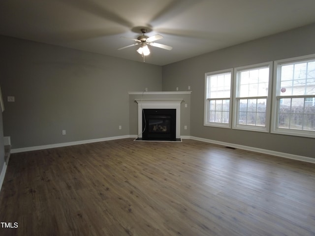 unfurnished living room featuring baseboards, a fireplace, ceiling fan, and dark wood finished floors