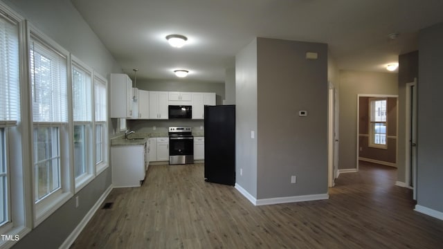 kitchen featuring black appliances, wood finished floors, baseboards, and a sink